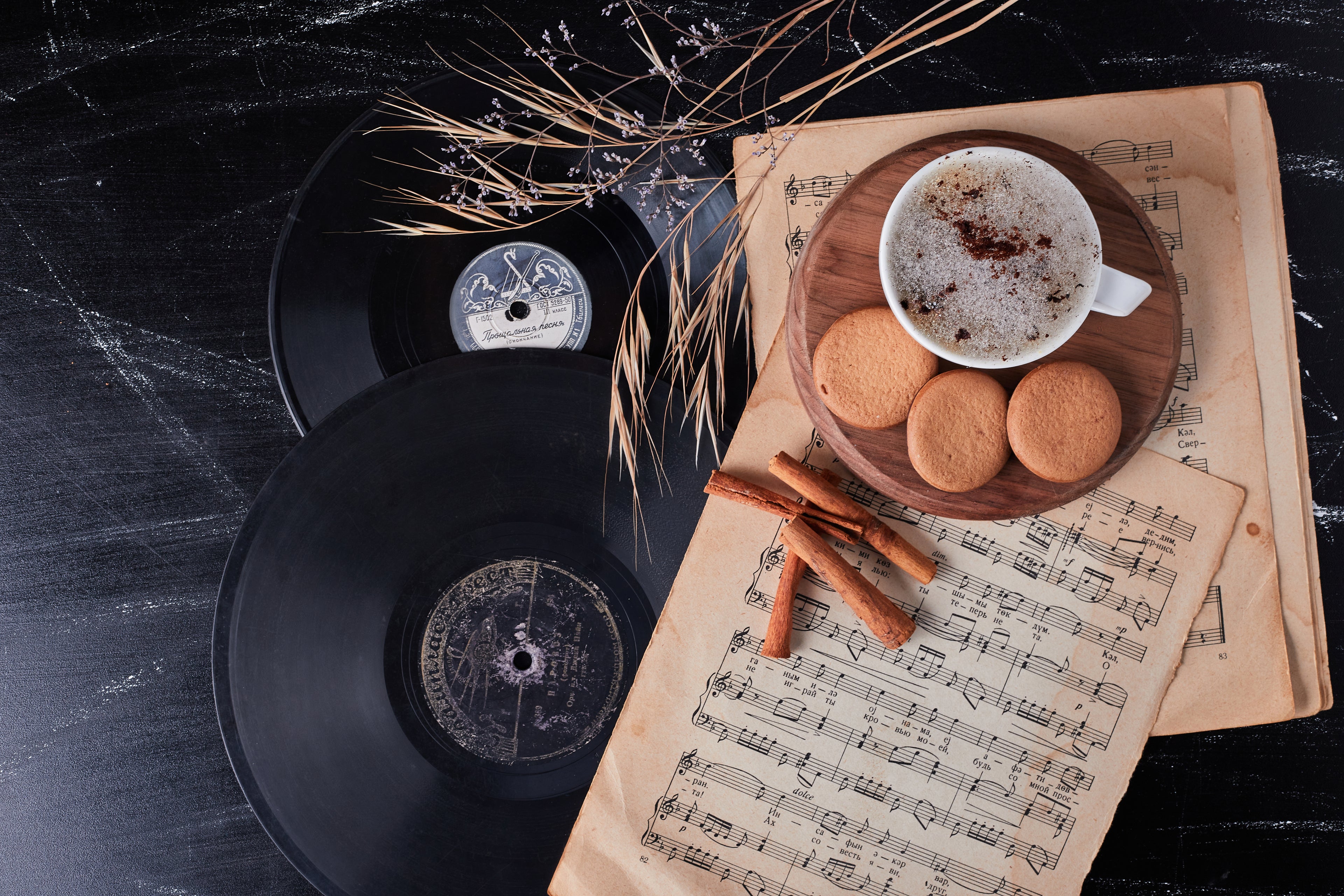 Black vinyl records with a cup of coffee and cookies on a sheet of music, on a dark surface.