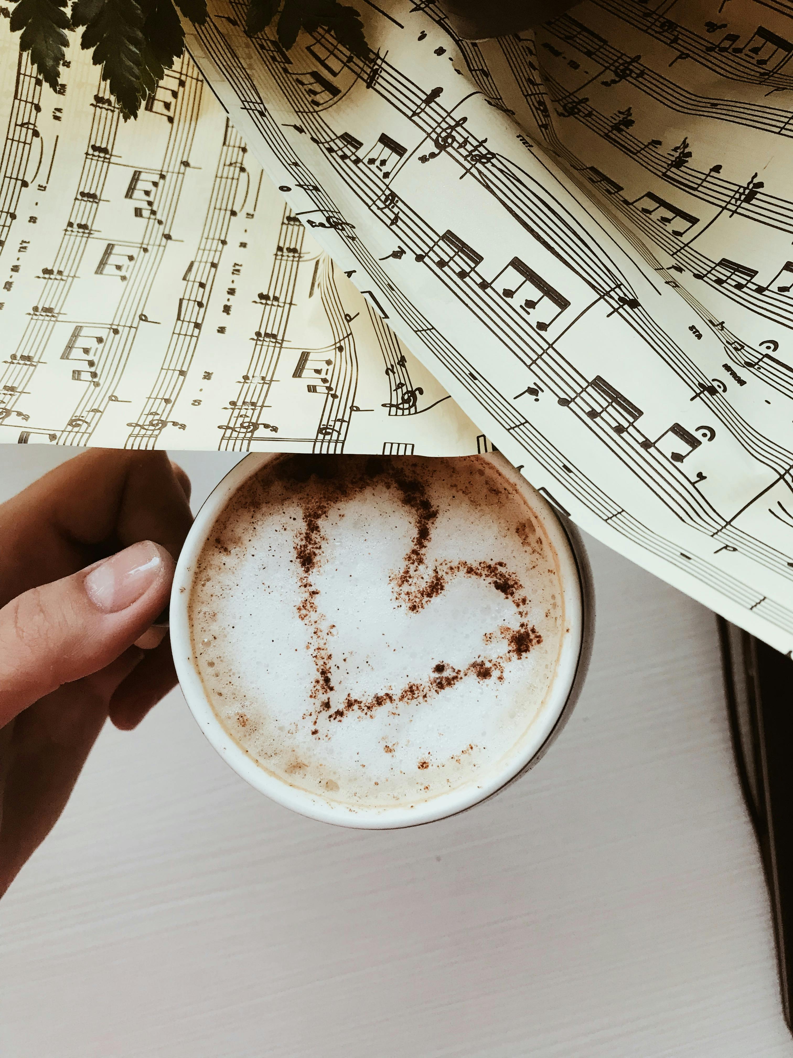 Hand holding a cup of coffee with a heart design surrounded by sheet music.